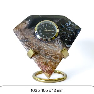 May include: A decorative quartz clock with a diamond-shaped stone base. The base features a mix of brown, black, and white patterns. The clock face is black with Roman numerals and a silver bezel. The clock measures 4 x 4.1 x 0.5 inches.