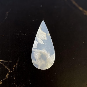 May include: A teardrop-shaped gemstone with a cloudy, sky-blue and white pattern. The stone has a polished surface and a pointed top. The overall effect is reminiscent of clouds in the sky. This gemstone is suitable for jewelry making.