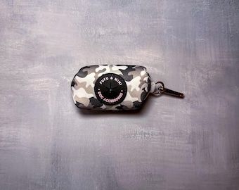 Puede incluir: Un dispensador de bolsas para recoger excrementos de perros con estampado de camuflaje y un logotipo circular negro que dice "Fufu & Mini Dog Accessories".