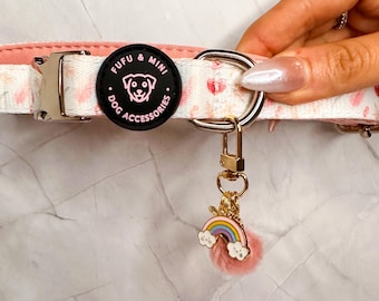 Puede incluir: Un collar de perro rosa y blanco con una etiqueta redonda negra que dice "Fufu & Mini Dog Accessories". Un amuleto dorado con un arcoíris y nubes está unido al collar.