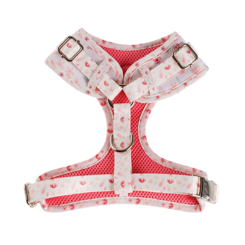 Puede incluir: Un arn&eacute;s para perro rosa y blanco con un patr&oacute;n floral. El arn&eacute;s tiene un forro de malla y dos hebillas ajustables.