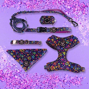 May include: A colorful dog harness, collar, leash, and bandana set with a peace sign and flower pattern. The set is purple, blue, pink, yellow, and green.
