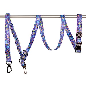 May include: A set of three dog accessories in a blue, pink, and yellow peace sign and flower pattern. The set includes a leash, a retractable leash, and a collar.