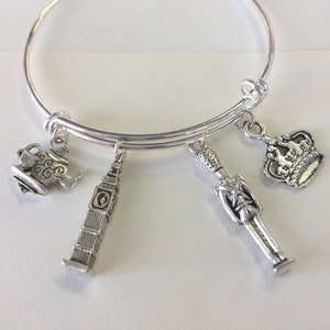 May include: Silver-toned charm bracelet featuring four dangling charms: a teapot, Big Ben, a British guard, and a crown. The bracelet is a simple, adjustable bangle style, perfect for adding a touch of British flair to any outfit.