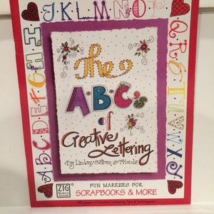 May include: A book titled "The ABC of Creative Lettering" with a red border. The cover features colorful lettering and floral accents. The book is designed for scrapbooks and more, with 40 pages of lettering tips and techniques.