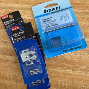 May include: Three packages of replacement hardware for drawers. Two packages are labeled "Roller Catch" and "Zinc Plated". The third package is labeled "Drawer Replacement Hardware" and "Drawer track backplate".