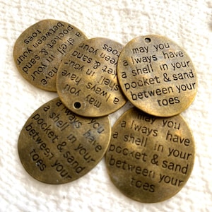 May include: Several bronze-colored, oval-shaped charms with the engraved text "May you always have a shell in your pocket & sand between your toes." The charms have a hole at the top for stringing.