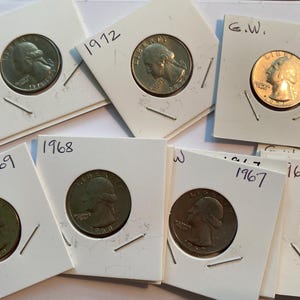 May include: A collection of U.S. quarter coins, each encased in a white cardboard holder. The years 1976, 1972, 1971, 1969, 1968, 1967, and 1965 are visible on the holders. The coins feature the profile of George Washington.