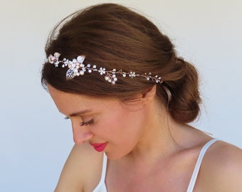 May include: A delicate gold headband with a floral design featuring pink and white flowers, leaves, and pearls. The headband is worn by a person with brown hair.
