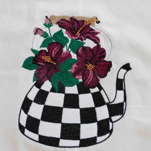 May include: Embroidered teapot design featuring a black and white checkered pattern on the body. The teapot is filled with burgundy hibiscus flowers and green leaves. The background is a plain white fabric.
