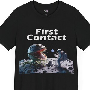 May include: Black t-shirt with a graphic print of an astronaut meeting a large, toothy, green alien on the moon. The text "First Contact" is printed above the image.