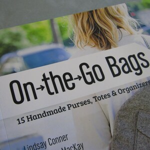 May include: A white and gray fabric tote bag with the text "On-the-Go Bags" and "15 Handmade Purses, Totes & Organizers".