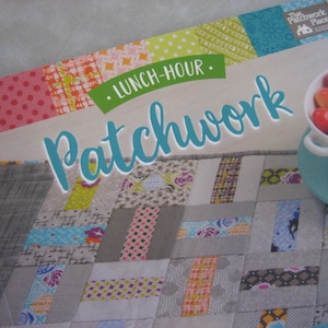 May include: A book titled "Lunch-Hour Patchwork" with a colorful patchwork quilt design on the cover. The book is published by The Patchwork Place.