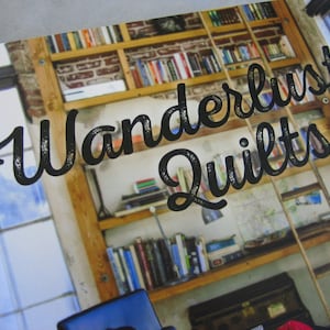 May include: A close-up of a wooden bookshelf filled with books. The bookshelf has a sign that reads "Wanderlust Quilts".