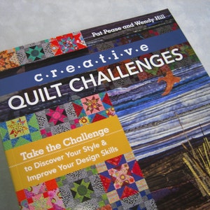 May include: Book cover with a blue background and the title "creative QUILT CHALLENGES". The cover features a variety of colorful quilt blocks and a close-up of a quilt with a blue and white striped pattern.