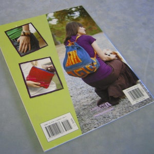 May include: The back cover of a book titled "Leisure Arts" featuring a woman wearing a colorful drawstring bag with a dog in her arms. The book cover also features a close-up of a red and blue fabric bag and a close-up of a person wearing a watch and a blue shirt.