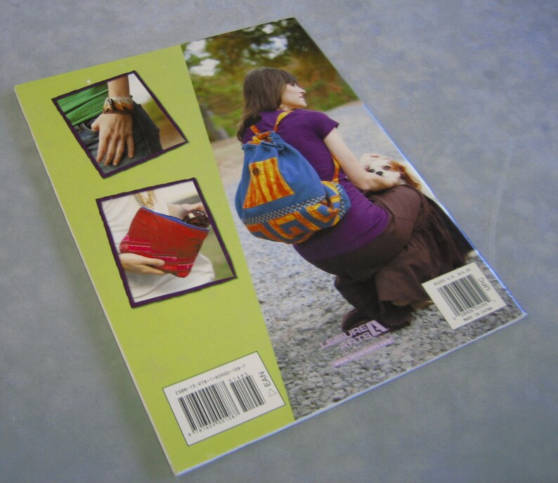 May include: The back cover of a book titled "Leisure Arts" featuring a woman wearing a colorful drawstring bag with a dog in her arms. The book cover also features a close-up of a red and blue fabric bag and a close-up of a person wearing a watch and a blue shirt.