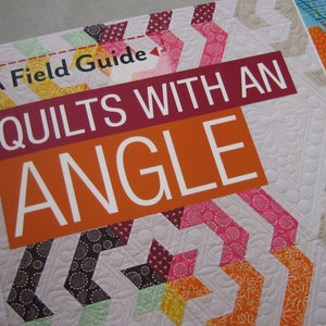 May include: A Field Guide to Quilts With An Angle. The book cover features a white quilt with colorful chevron patterns in pink, yellow, and brown. The title is in large white letters on a maroon and orange background.