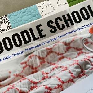 May include: A book titled "Doodle School: A Daily Design Challenge to Up Your Free-Motion Quilting Game" with a white background and a red and white quilt on top.