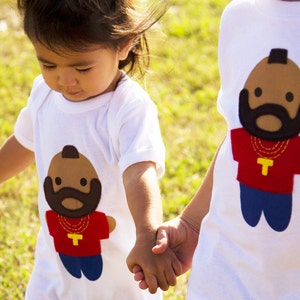 Puede incluir: Dos ni&ntilde;os con camisetas blancas con im&aacute;genes de dibujos animados de un hombre con barba y una cadena de oro. Los ni&ntilde;os se est&aacute;n dando la mano.
