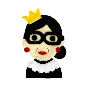 May include: Felt appliqué of a person wearing a black robe, a white collar, and a yellow crown. The person has black hair, black glasses, red earrings, and a red mouth.
