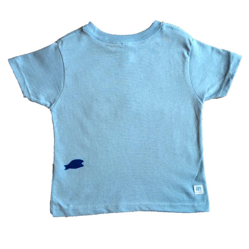 Op de afbeelding: Een lichtblauw T-shirt met korte mouwen en een klein blauw visontwerp aan de linkerkant. Het shirt heeft een wit label met het woord "600" erop.