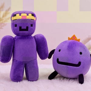 Könnte beinhalten: Ein violettes Plüschtier mit einem blockartigen, pixeligen Kopf und einer gelb-rosa Krone, neben einer runden, violetten Plüschfigur mit schwarzen Gliedmaßen und einer kleinen orangefarbenen Krone. Beide Spielzeuge haben einfache, dunkle Gesichtszüge.