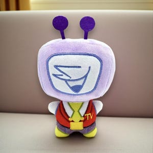 May include: A plush toy shaped like a cartoon character with a TV head. The toy is primarily lavender with a white screen displaying a stylized face. It wears a red vest, yellow shirt, and purple pants. Two purple antennae extend from the top of the head.
