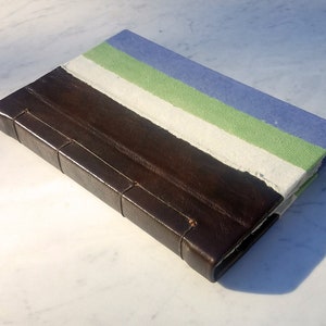 Puede incluir: Un diario encuadernado en cuero marrón con una cubierta de papel hecho a mano con rayas blancas, verdes y azules.