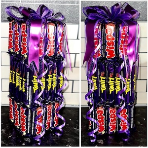 May include: A tower of chocolate bars wrapped in purple foil and tied with purple ribbon. The bars are labeled "Wispa" and "Twirl".