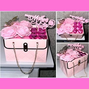 Pode incluir: Uma caixa de presente rosa com alça de corrente dourada, cheia de rosas cor-de-rosa e chocolates em forma de coração rosa. A caixa tem uma placa que diz "Happy Mother's Day" no topo.