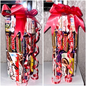 May include: A tower of assorted chocolate bars wrapped in red ribbon. The bars include Wispa, Crunchie, Galaxy, Kinder, and Bueno.