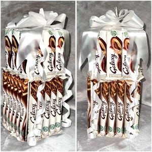 May include: A tower of Galaxy chocolate bars wrapped in white ribbon. The bars are stacked in a tower and tied with a white ribbon. The bars are all Galaxy brand chocolate.