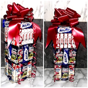 May include: A tower of assorted chocolate bars wrapped in red ribbon. The tower includes Milky Way, Kinder, and Freddo chocolate bars.