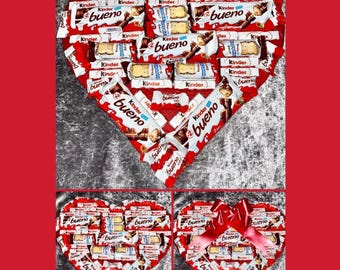 May include: A heart-shaped arrangement of chocolate bars, featuring Kinder Bueno brand chocolate. The bars are arranged in a heart shape and are wrapped in red and white foil. The words "Kinder Bueno" are visible on the chocolate bars.