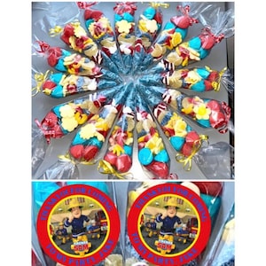 May include: A collection of clear plastic cones filled with colorful candies, decorated with yellow ribbon and a red and yellow circular sticker featuring a cartoon firefighter character from the show "Fireman Sam" with the text "Thank you for coming to my party, Jake".