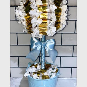 May include: A blue candy tree with a blue ribbon bow and a blue bucket filled with wrapped sweets. The sweets are wrapped in white paper and have the text "Werther's Original" printed on them.
