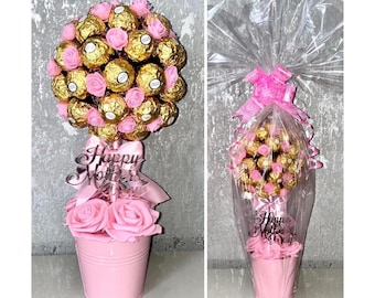 May include: A pink bucket filled with pink roses and a chocolate arrangement. The arrangement is topped with gold-wrapped chocolates and pink roses. A pink ribbon and a sign that says "Happy Mother's Day" are also included.