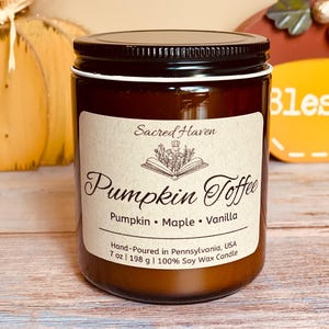 May include: A brown glass jar candle with a black lid and a white label. The label reads "Sacred Haven Pumpkin Toffee" with the scent notes of pumpkin, maple, and vanilla. The candle is 7 oz (198 g) and made of 100% soy wax.