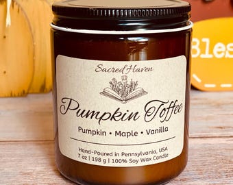 May include: A brown glass jar candle with a black lid and a white label. The label reads "Sacred Haven Pumpkin Toffee" with the scent notes of pumpkin, maple, and vanilla. The candle is 7 oz (198 g) and made of 100% soy wax.
