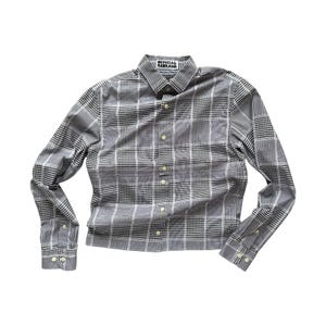 May include: A gray and white plaid button-down shirt with long sleeves. The shirt has a classic collar and buttoned cuffs. The text "OFFICIAL REBRAND" is printed on the collar.