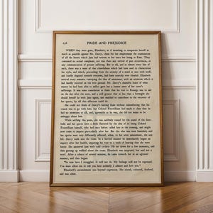 Puede incluir: Impresión enmarcada de una página del libro "Orgullo y Prejuicio" de Jane Austen. El texto en tinta negra sobre papel envejecido, enmarcado en madera. La impresión se muestra contra una pared blanca con molduras decorativas y suelo de madera.