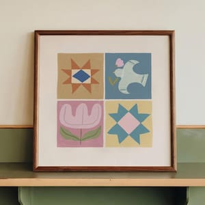 Può includere: Una stampa quadrata incorniciata che presenta quattro pannelli distinti con illustrazioni di una stella geometrica, un uccello con un piccolo fiore rosa, un tulipano stilizzato e un motivo a stella blu e giallo, in una cornice in legno.