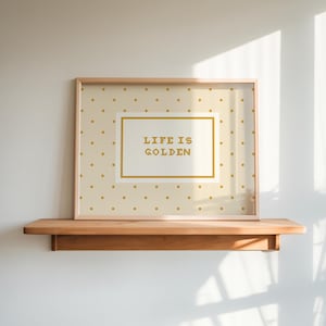 Puede incluir: Una impresi&oacute;n rectangular enmarcada con un fondo beige claro y un patr&oacute;n repetitivo de peque&ntilde;os puntos dorados. En el centro, un panel rectangular blanco con un borde dorado muestra el texto "LIFE IS GOLDEN" en letras doradas.