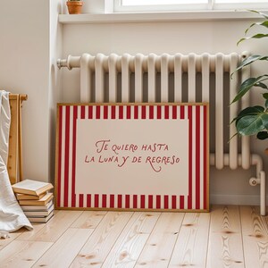 May include: A framed artwork with a red and white striped border. The artwork features the text "Te quiero hasta la luna y de regreso" in red script on a white background. The frame is made of wood.