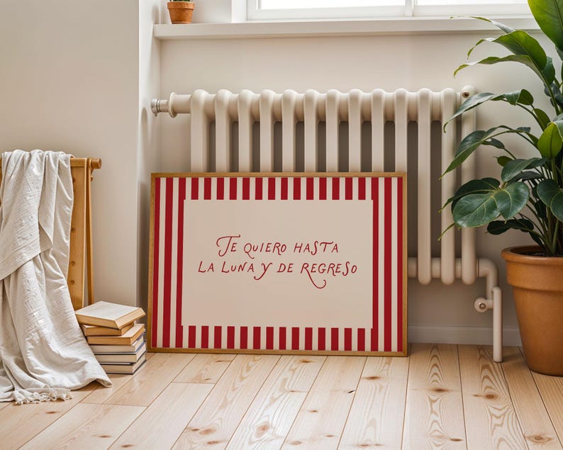 May include: A framed artwork with a red and white striped border. The artwork features the text "Te quiero hasta la luna y de regreso" in red script on a white background. The frame is made of wood.