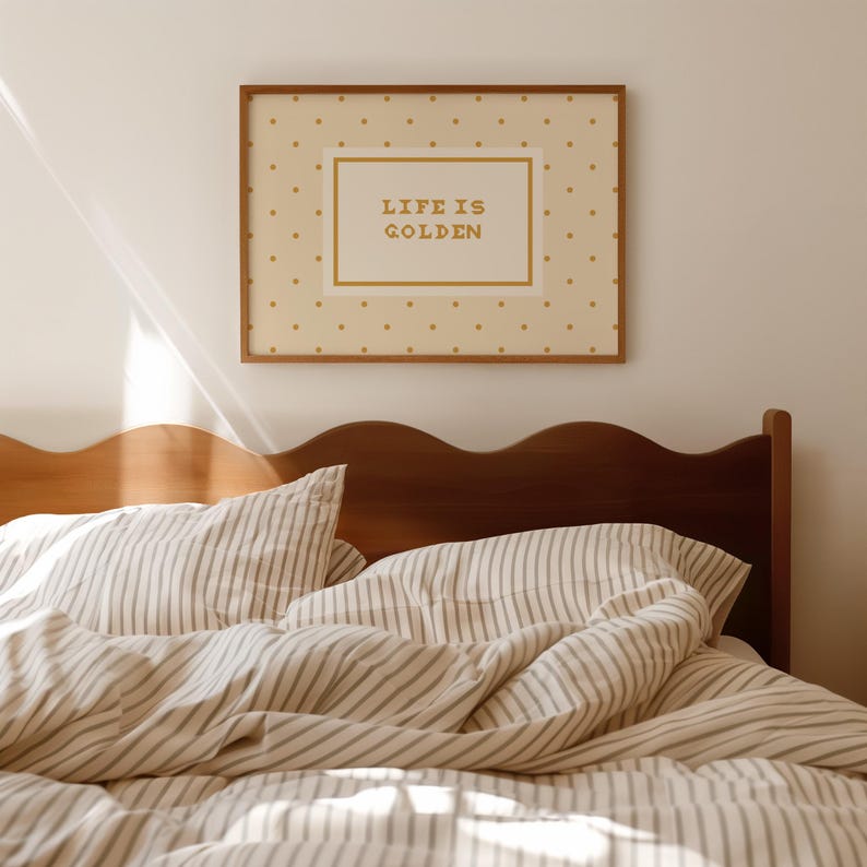 Puede incluir: Un cuadro rectangular enmarcado con fondo crema y un patr&oacute;n de peque&ntilde;os puntos dorados. Centrado hay un borde rectangular que contiene el texto "LIFE IS GOLDEN" en letras doradas, exhibido sobre un cabecero de madera.
