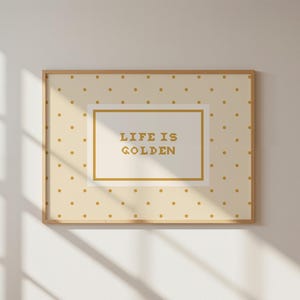 Puede incluir: Una l&aacute;mina decorativa rectangular en un marco de madera clara con fondo crema y un patr&oacute;n repetitivo de peque&ntilde;os puntos dorados. En el centro, un recuadro blanco con borde dorado contiene el texto en color oro "LIFE IS GOLDEN".