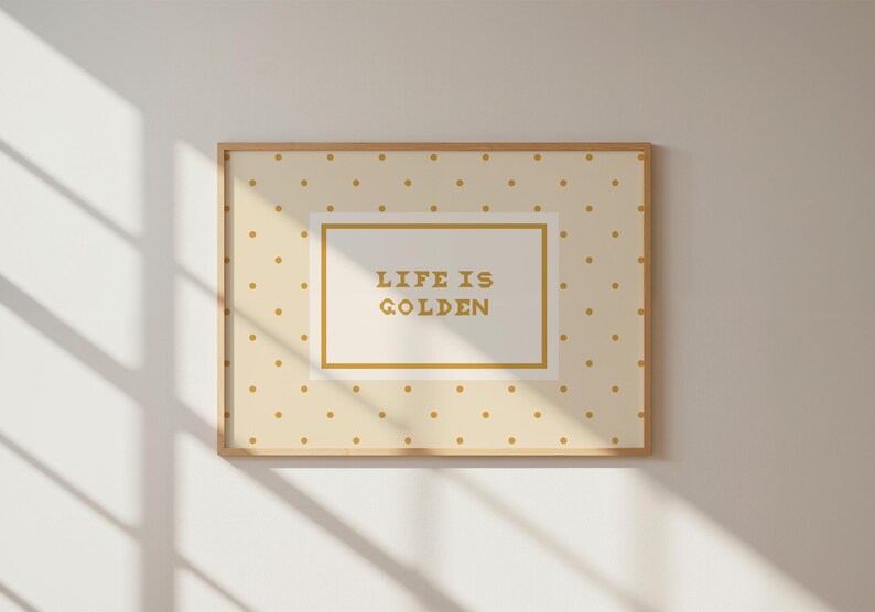 Puede incluir: Una l&aacute;mina decorativa rectangular en un marco de madera clara con fondo crema y un patr&oacute;n repetitivo de peque&ntilde;os puntos dorados. En el centro, un recuadro blanco con borde dorado contiene el texto en color oro "LIFE IS GOLDEN".