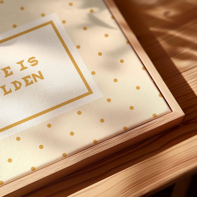 Puede incluir: Un lienzo enmarcado con un fondo de color crema claro y un patr&oacute;n de peque&ntilde;os puntos dorados. Un borde rectangular blanco central encierra el texto dorado que dice LIFE IS GOLDEN. La obra de arte est&aacute; dentro de un marco de madera clara.